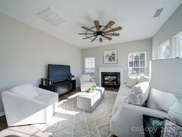 living room with a high end fireplace, light wood-type flooring, and ceiling fan