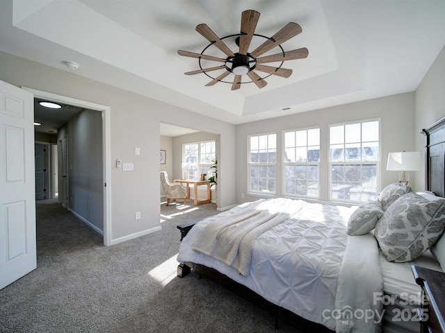 bedroom featuring a tray ceiling, carpet floors, multiple windows, and connected bathroom