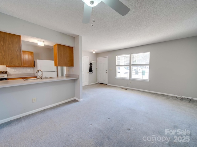 kitchen featuring light countertops, brown cabinetry, freestanding refrigerator, a sink, and baseboards