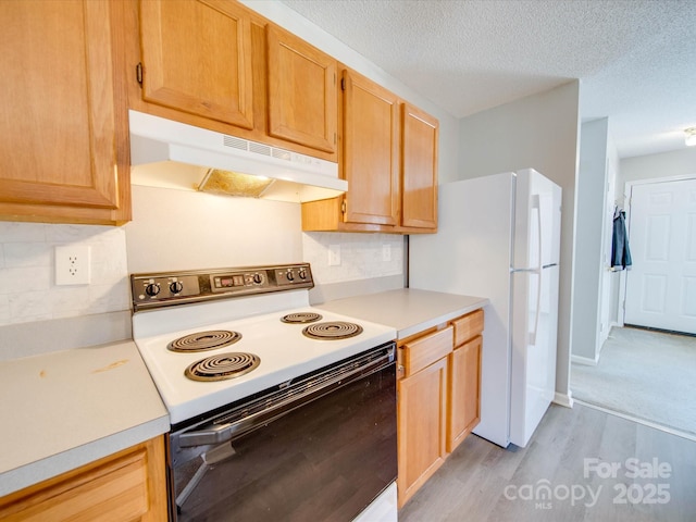 kitchen with electric range oven, light countertops, freestanding refrigerator, and under cabinet range hood