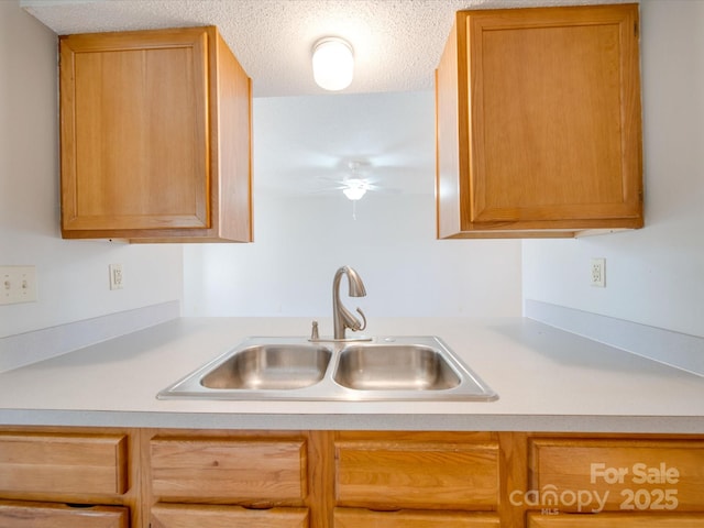 kitchen featuring a ceiling fan, light countertops, a sink, and a textured ceiling