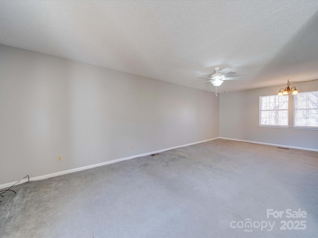 carpeted empty room with a textured ceiling, ceiling fan with notable chandelier, visible vents, and baseboards