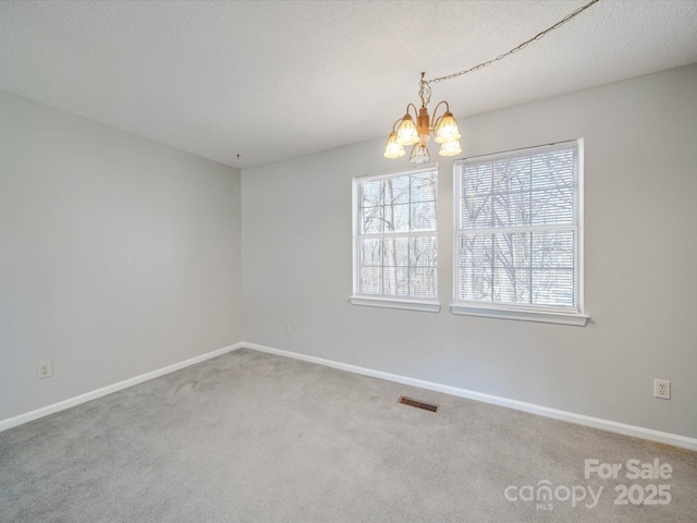 carpeted empty room with a chandelier, a textured ceiling, visible vents, and baseboards