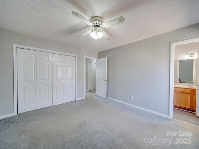 unfurnished bedroom featuring baseboards, connected bathroom, light colored carpet, a textured ceiling, and a closet