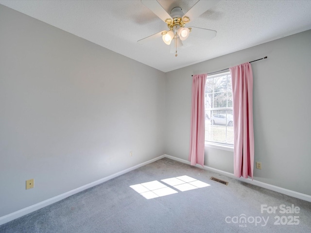 carpeted empty room featuring ceiling fan, a textured ceiling, visible vents, and baseboards