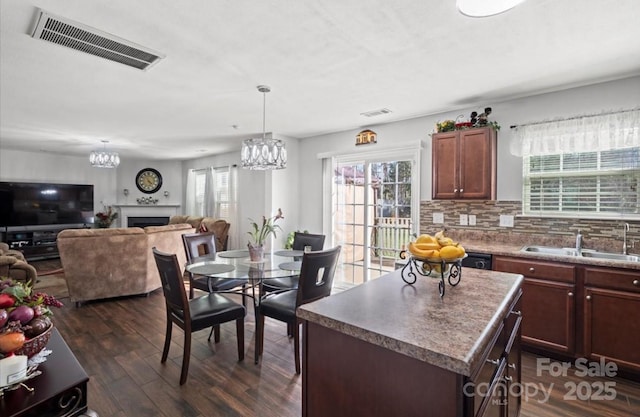 dining room with dark wood-style floors, visible vents, a fireplace, and a notable chandelier