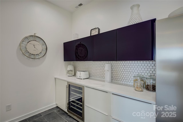 bar featuring beverage cooler, baseboards, visible vents, dark tile patterned flooring, and backsplash