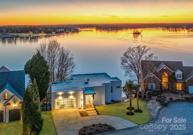 view of front of home featuring a garage, a water view, driveway, a yard, and stucco siding