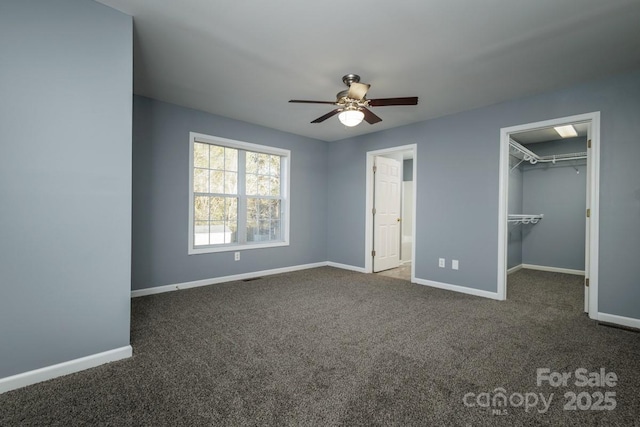 unfurnished bedroom with ceiling fan, dark colored carpet, a closet, and a spacious closet