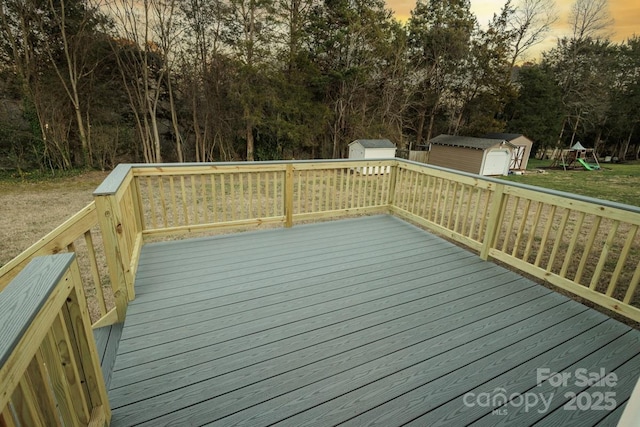 deck at dusk featuring a yard, a playground, and a storage shed