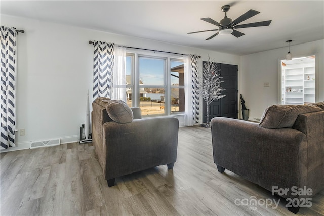 living area featuring baseboards, wood finished floors, visible vents, and a ceiling fan