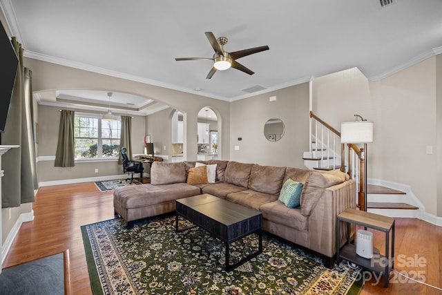 living room with baseboards, stairway, a tray ceiling, wood finished floors, and arched walkways