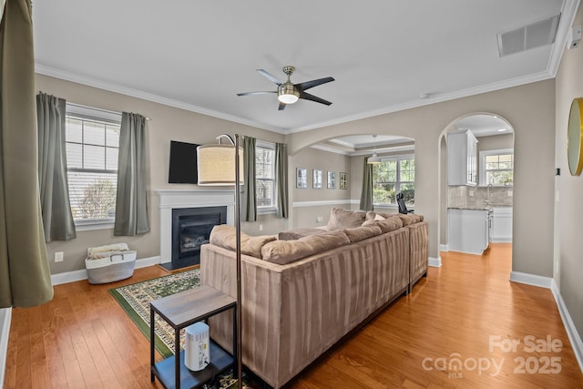 living area with visible vents, light wood finished floors, a fireplace with flush hearth, ceiling fan, and ornamental molding