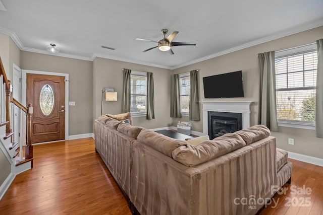 living area with visible vents, ornamental molding, wood finished floors, a glass covered fireplace, and stairway