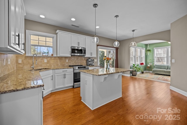 kitchen featuring backsplash, light wood-style floors, arched walkways, stainless steel appliances, and a sink