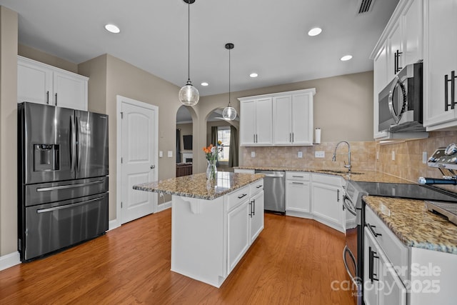 kitchen featuring visible vents, light wood-style flooring, arched walkways, a sink, and stainless steel appliances