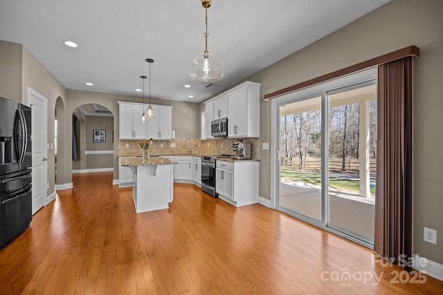 kitchen with tasteful backsplash, a kitchen island, stainless steel appliances, white cabinets, and light wood finished floors