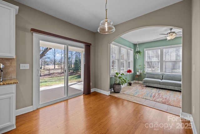 interior space with a wealth of natural light, baseboards, arched walkways, and light wood finished floors