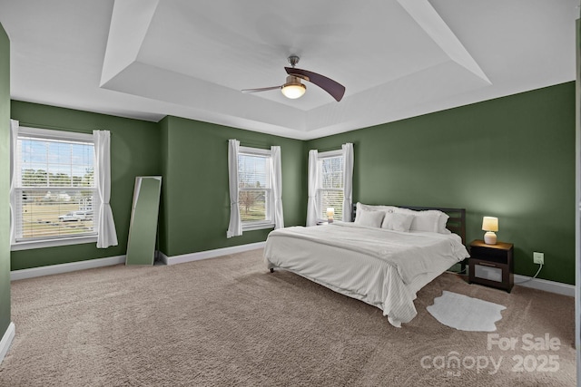 carpeted bedroom featuring multiple windows, baseboards, a tray ceiling, and a ceiling fan