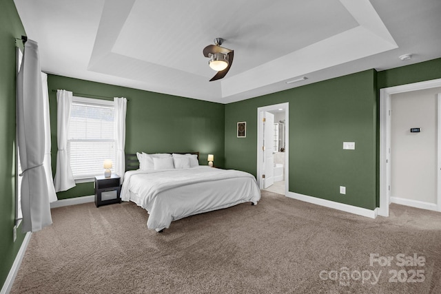 carpeted bedroom featuring a ceiling fan, visible vents, baseboards, ensuite bath, and a tray ceiling