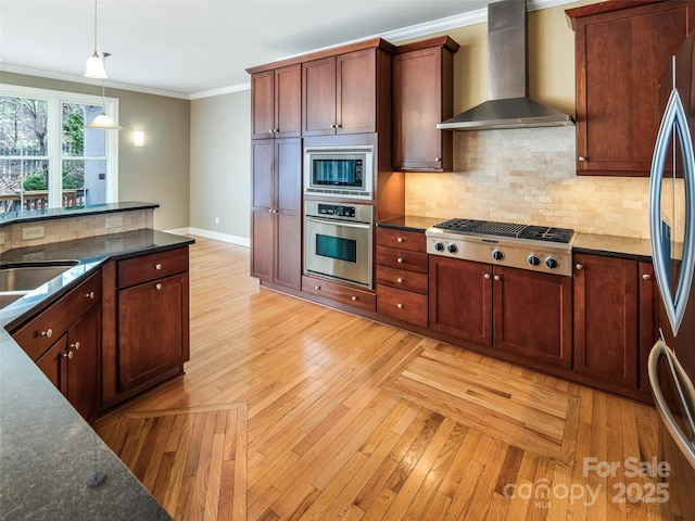 kitchen featuring light wood-type flooring, stainless steel appliances, ornamental molding, wall chimney range hood, and pendant lighting