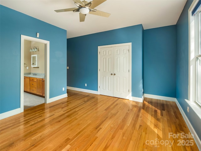 unfurnished bedroom featuring ceiling fan, light hardwood / wood-style flooring, ensuite bath, and a closet