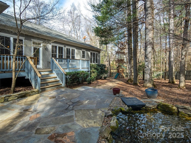 rear view of property featuring a wooden deck, a playground, and a patio area