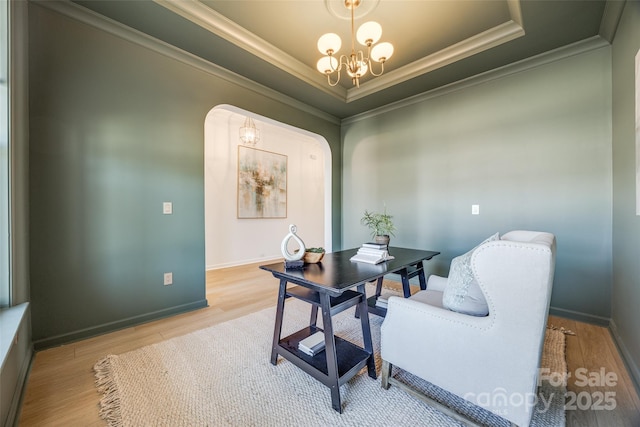 office featuring arched walkways, a raised ceiling, an inviting chandelier, ornamental molding, and wood finished floors