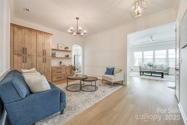 living area featuring visible vents, arched walkways, light wood-style flooring, ornamental molding, and a decorative wall