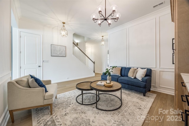 living room featuring visible vents, a decorative wall, stairway, an inviting chandelier, and wood finished floors