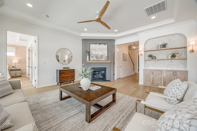 living area featuring visible vents, a fireplace with flush hearth, crown molding, light wood-type flooring, and recessed lighting