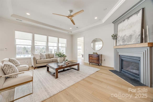 living area with a fireplace with flush hearth, visible vents, ornamental molding, light wood finished floors, and a raised ceiling