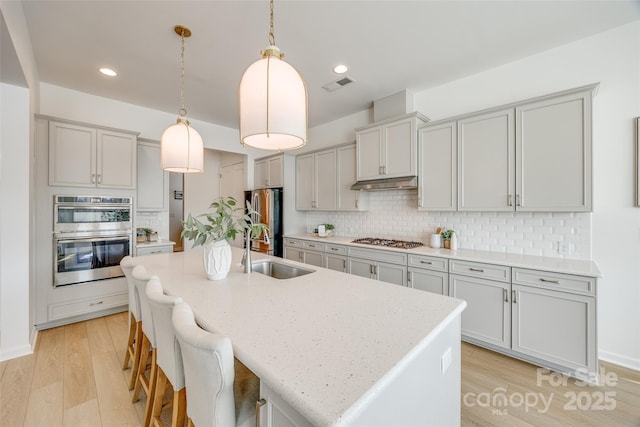 kitchen with tasteful backsplash, visible vents, appliances with stainless steel finishes, under cabinet range hood, and a sink