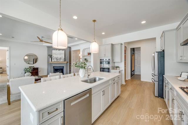 kitchen with appliances with stainless steel finishes, open floor plan, light wood-type flooring, a fireplace, and a sink