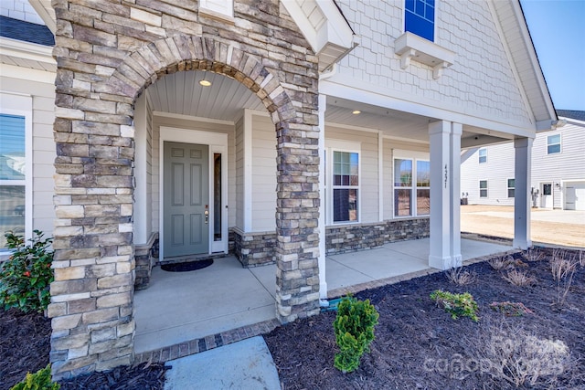 view of exterior entry with stone siding and covered porch