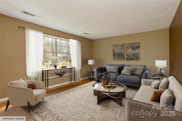 living area featuring a textured ceiling, wood finished floors, visible vents, and baseboards