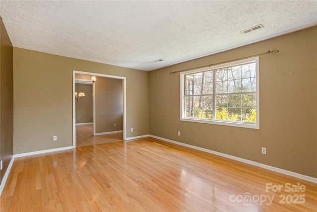 spare room with light wood-type flooring, visible vents, a textured ceiling, and baseboards