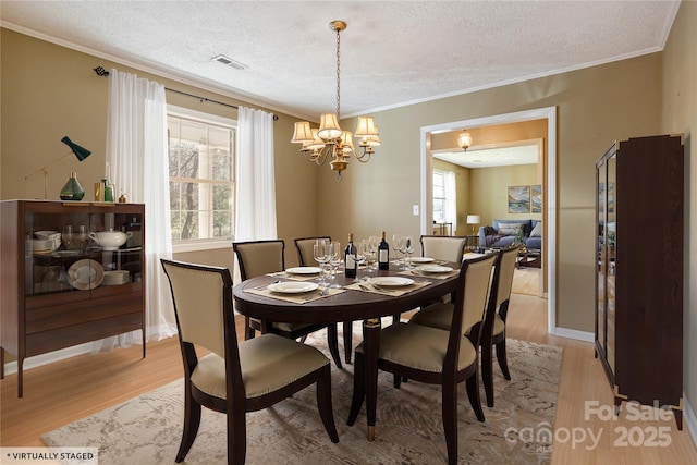 dining area with light wood-style floors, visible vents, crown molding, and a textured ceiling