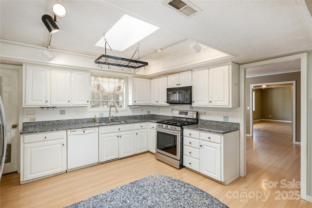 kitchen with a skylight, stainless steel gas stove, a sink, black microwave, and dishwasher