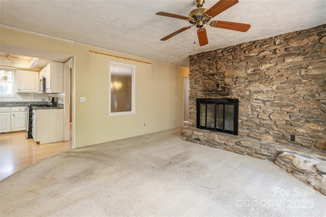 unfurnished living room featuring a ceiling fan, light colored carpet, a textured ceiling, and a stone fireplace