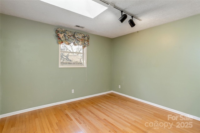 unfurnished room with light wood-type flooring, visible vents, a textured ceiling, and a skylight