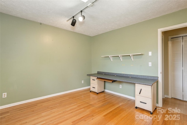 unfurnished office featuring light wood-style floors, built in study area, a textured ceiling, and baseboards