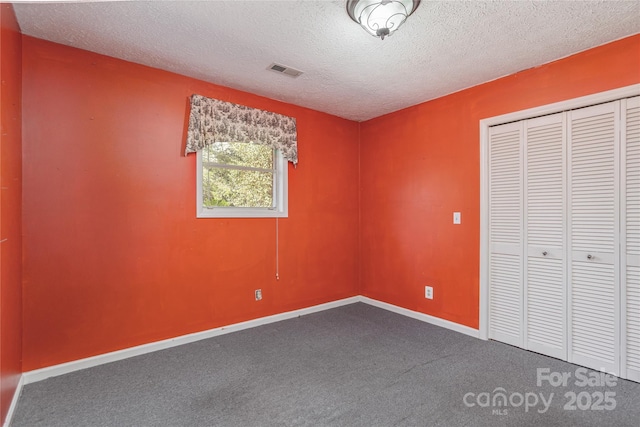 unfurnished bedroom featuring a textured ceiling, visible vents, baseboards, a closet, and dark colored carpet