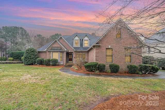 view of front of house featuring a shingled roof, brick siding, and a front lawn