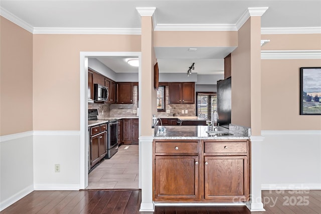 kitchen with tasteful backsplash, wood-type flooring, stainless steel appliances, light stone countertops, and kitchen peninsula