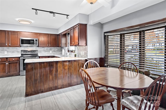 kitchen featuring kitchen peninsula, stainless steel appliances, dark brown cabinetry, sink, and decorative backsplash