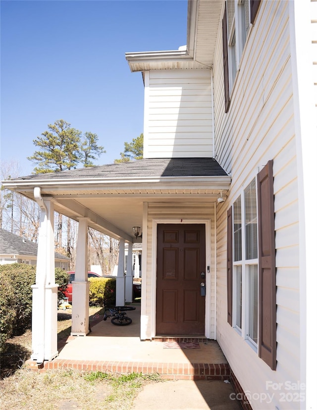 entrance to property with a porch and roof with shingles