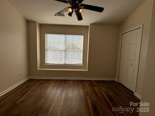 unfurnished bedroom with ceiling fan, dark hardwood / wood-style floors, a textured ceiling, and a closet