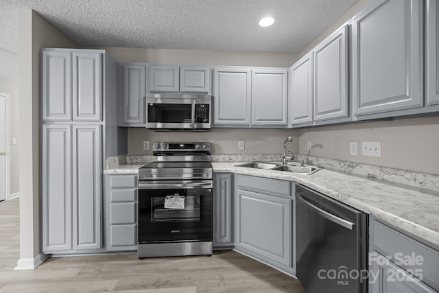 kitchen featuring a textured ceiling, stainless steel appliances, light wood-type flooring, and a sink