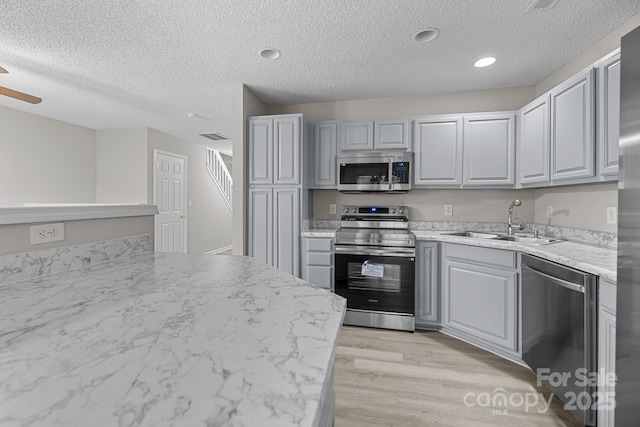 kitchen with stainless steel appliances, light countertops, light wood-style flooring, gray cabinetry, and a sink